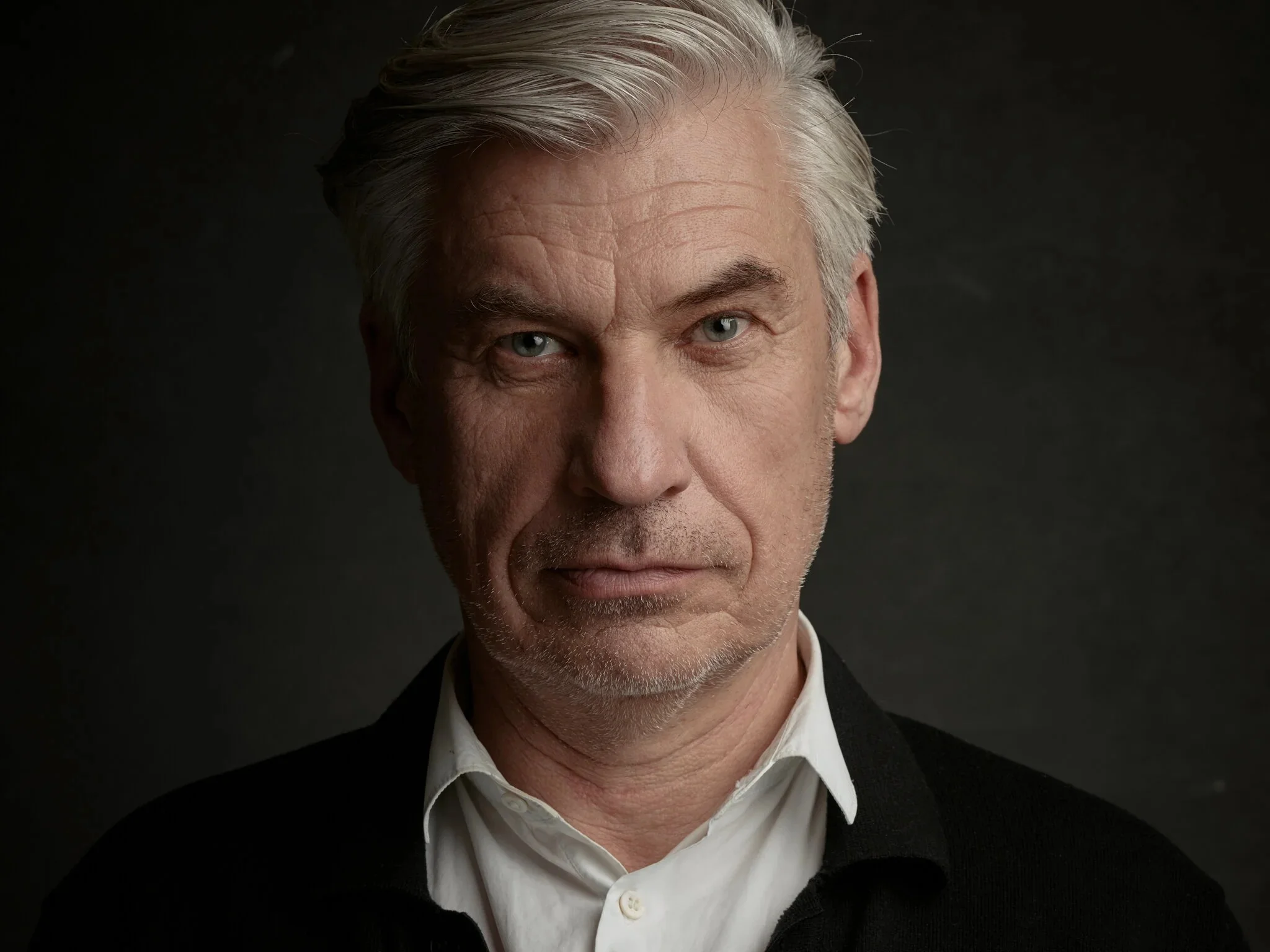 Front-facing studio portrait of a middle-aged man with grey hair and blue eyes.